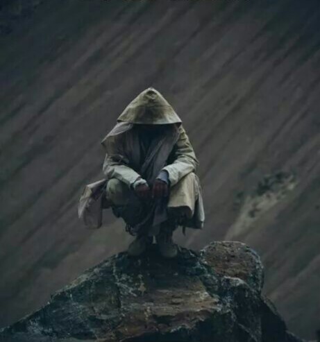 hooded figure in a long leather coat sitting crouched on the end of a rock with a river beneath him flowing diagonally across the image. a small island is visible on his right in the deep below.
